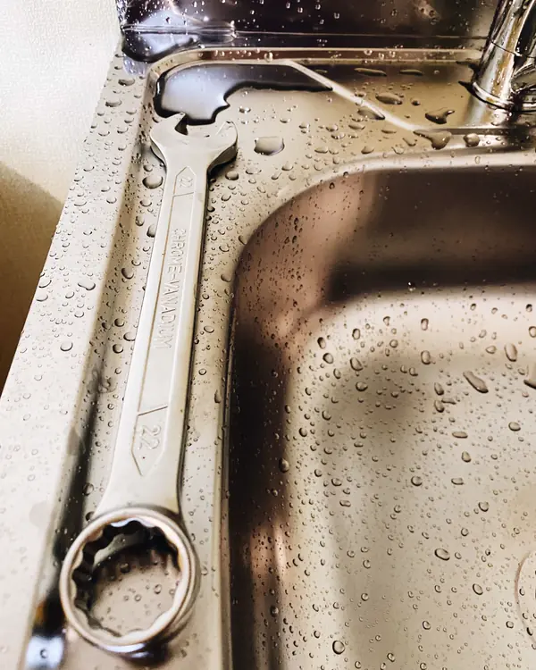 A wrench resting in a wet stainless steel kitchen sink