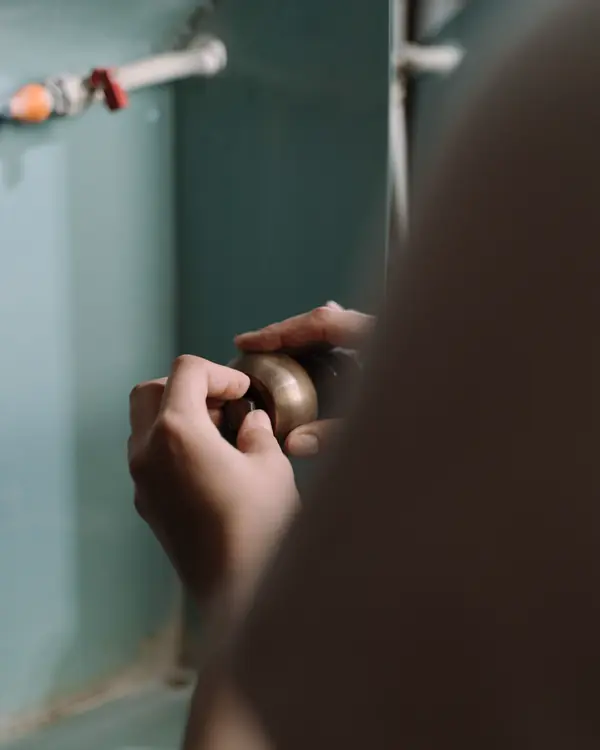 Hands turning a shutoff valve on a pipe under a sink