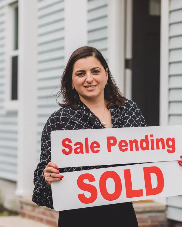 Dana Whitfield holding a sale pending sign in front of a house
