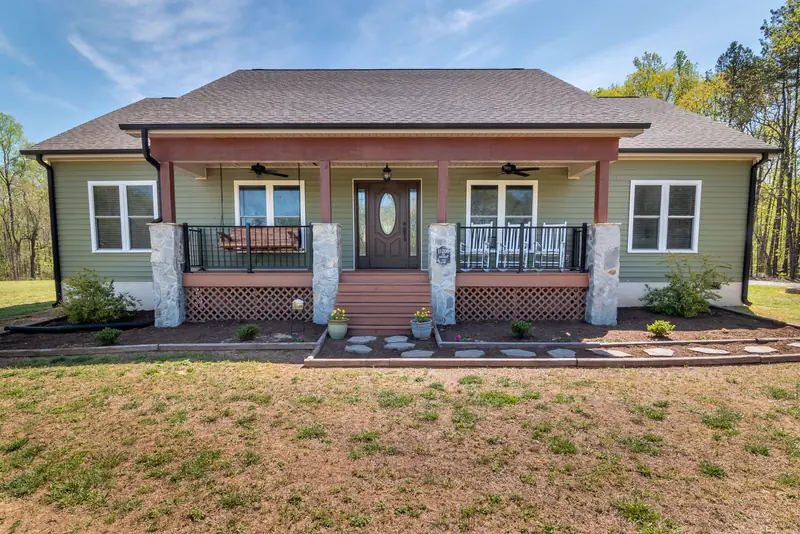 Single-story sage green ranch home with a wide front porch and a brick foundation