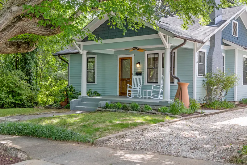 Sage green bungalow with white rocking chairs on a covered front porch