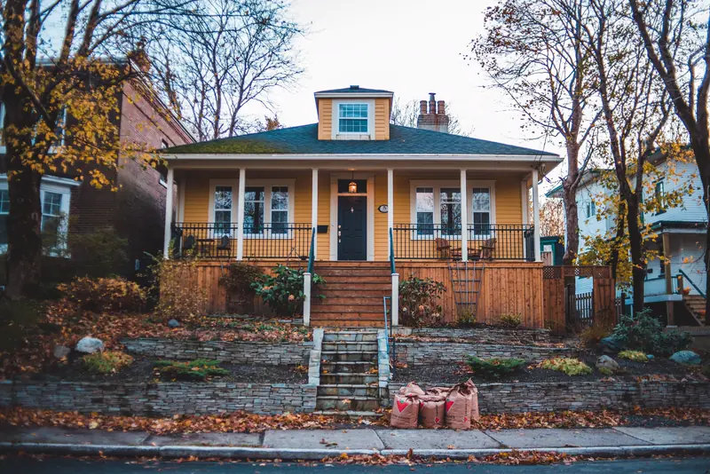 Yellow bungalow with a deep front porch and stone steps in autumn