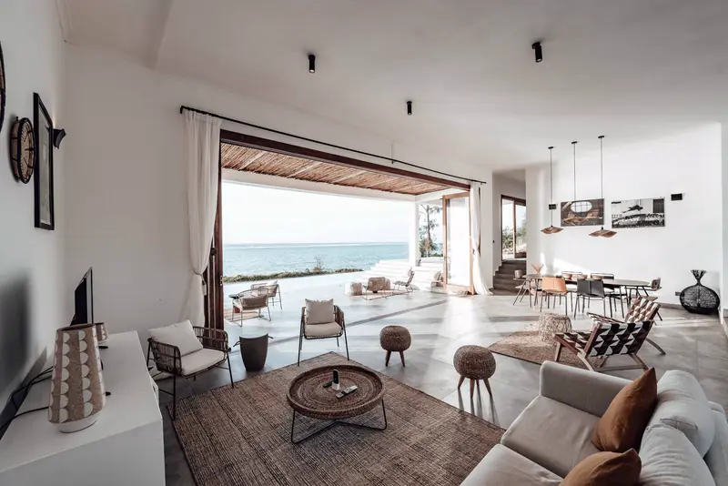 Open living room with low sofas and a wall of glass doors open to the water
