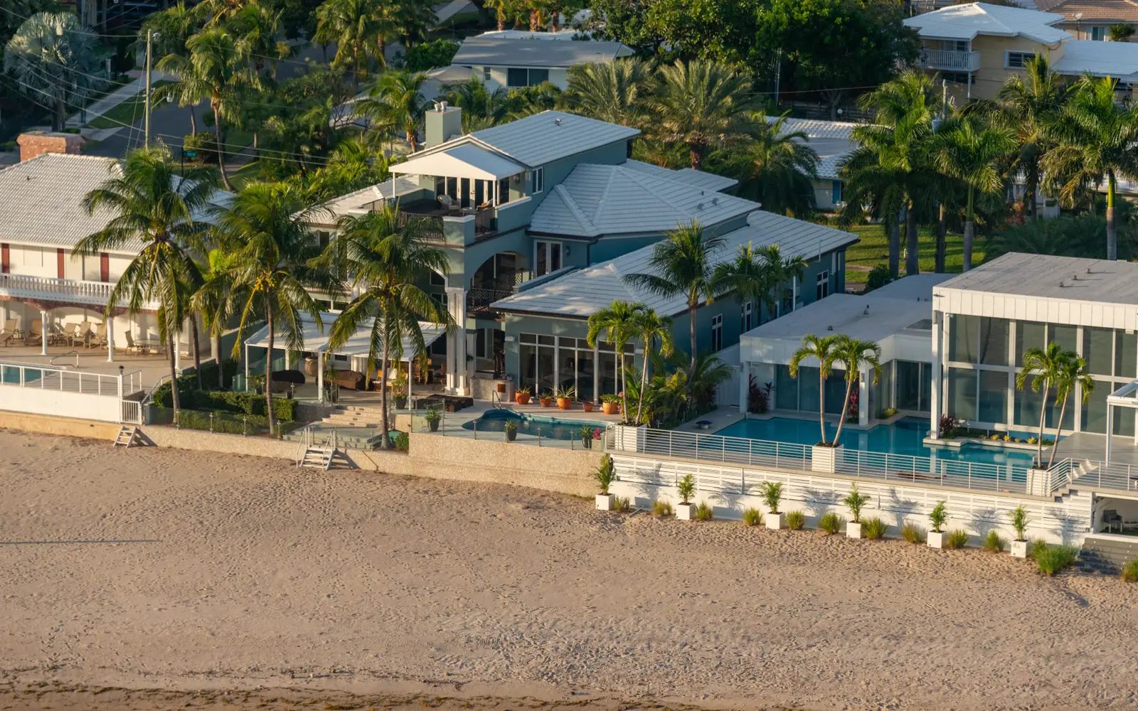 Gulf-front homes with pools and palm trees above a wide sand beach at golden hour