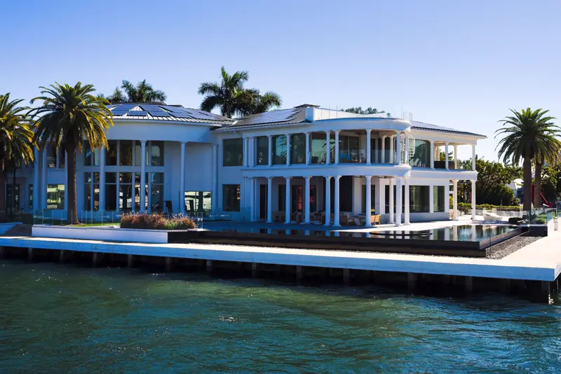 White modern home with wraparound terraces and an infinity pool on a wide canal