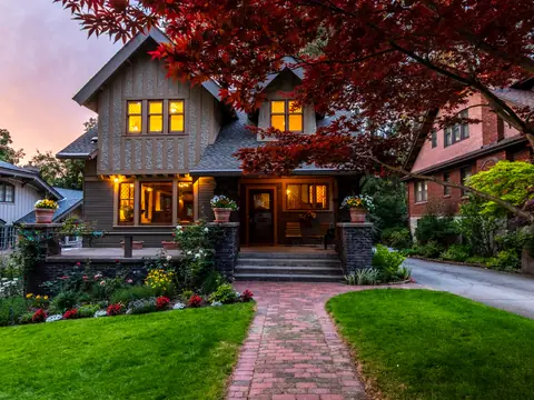 Craftsman house at dusk with lit windows, a brick path and a red maple