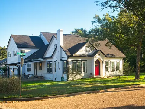 White cottage-style house with a steep roof and a red front door on a corner lot
