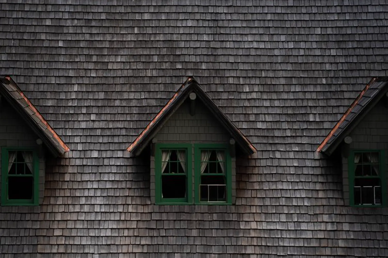 Weathered cedar shake roof with three dormers and green window frames