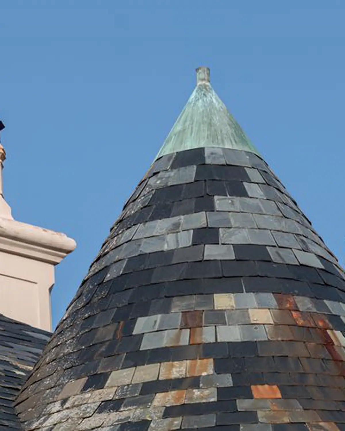 Conical slate turret with a green copper finial against a blue sky