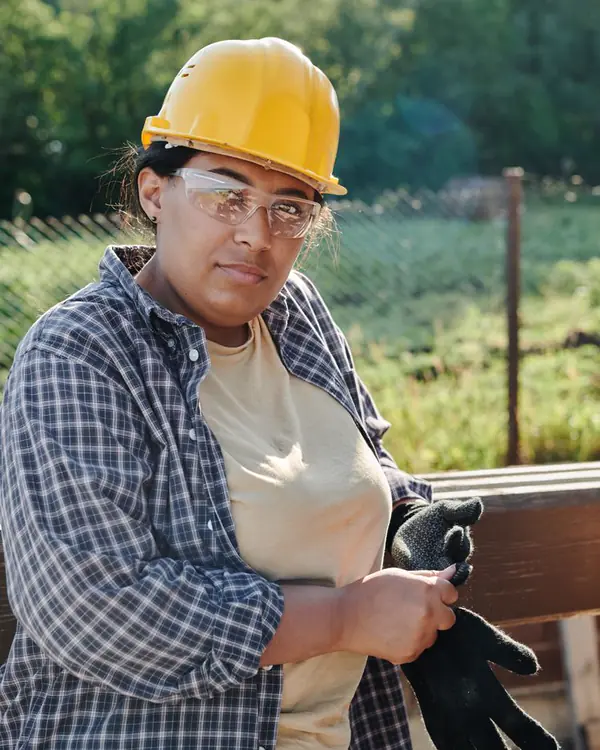 Nora Hagen in a yellow hard hat and plaid shirt, pulling on work gloves