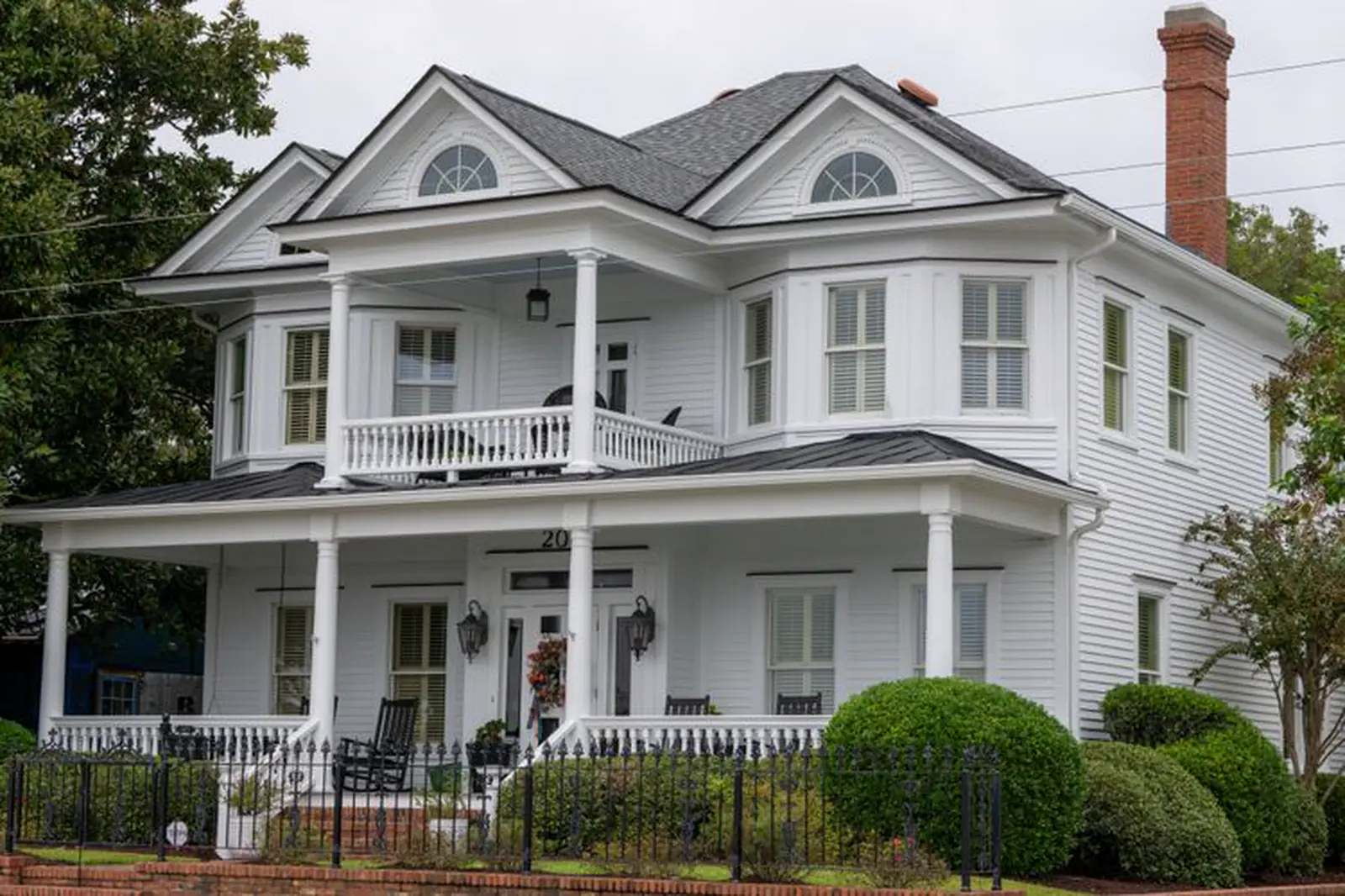 White two-story house with a wraparound porch and gray metal porch roofs