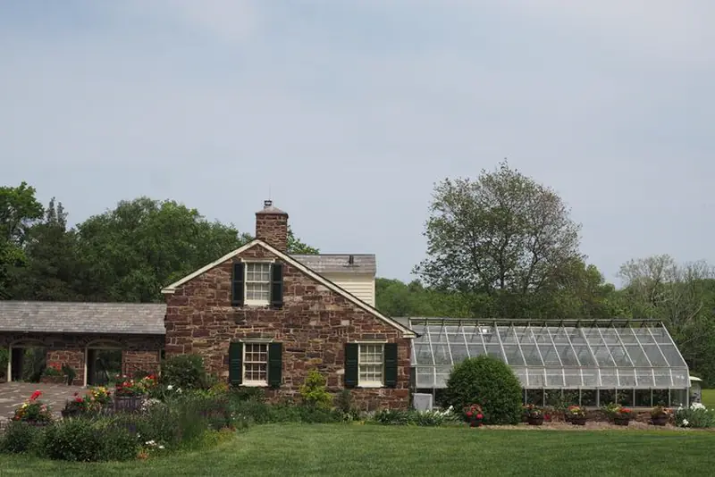Fieldstone farmhouse with a dark slate roof beside a greenhouse