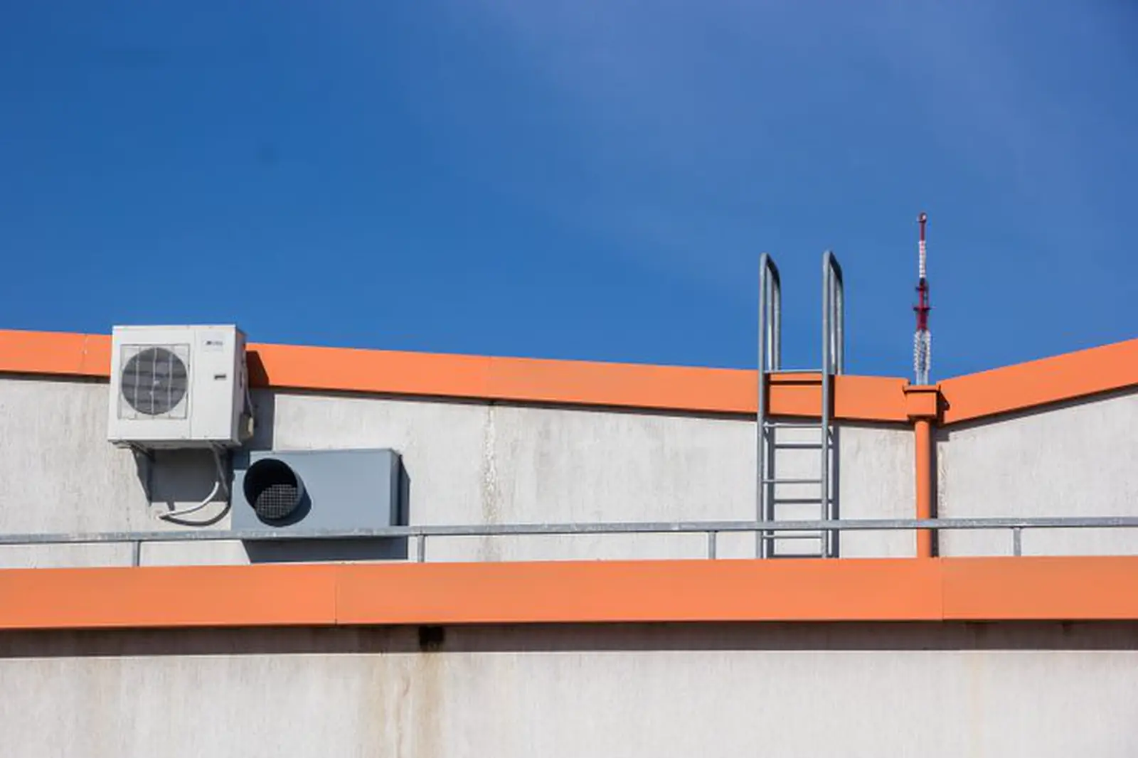 Rooftop condenser unit and roof access ladder on a white parapet with orange coping
