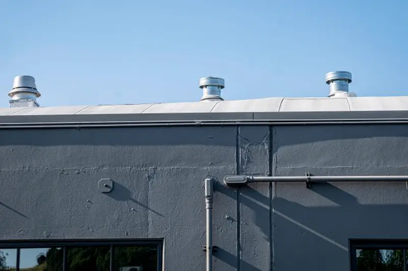 Gray building wall with three rooftop exhaust vents against a blue sky