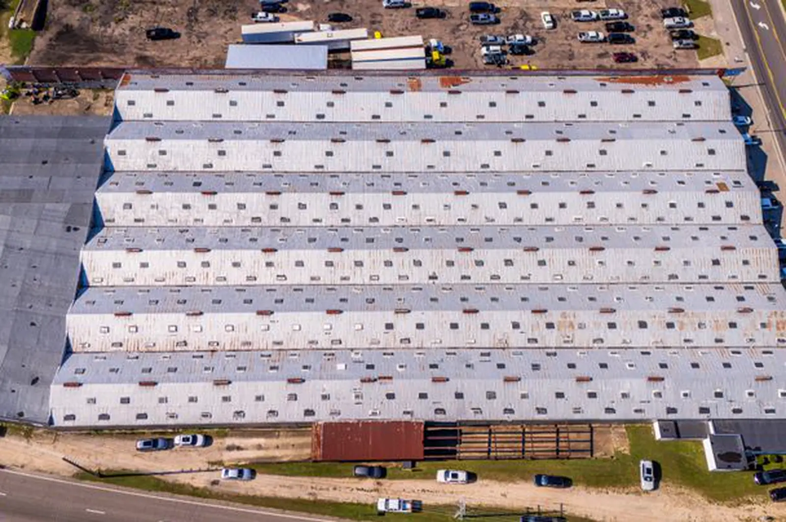 Aerial view of a long distribution warehouse roof beside a truck lot