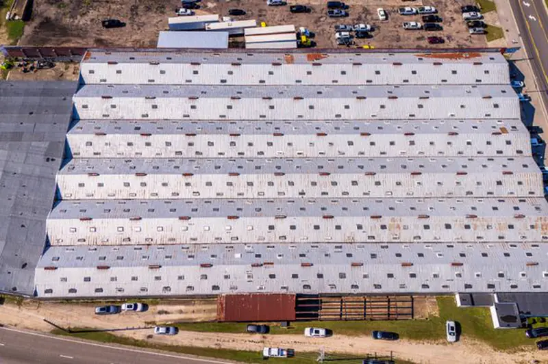 Aerial view of a long distribution warehouse with a metal roof and truck lot