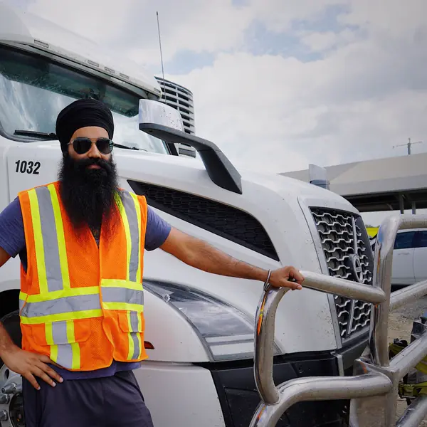 A truck driver in a safety vest stands beside his semi truck
