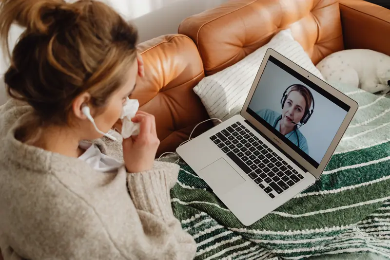 A woman with a cold talks to a provider on her laptop from the couch