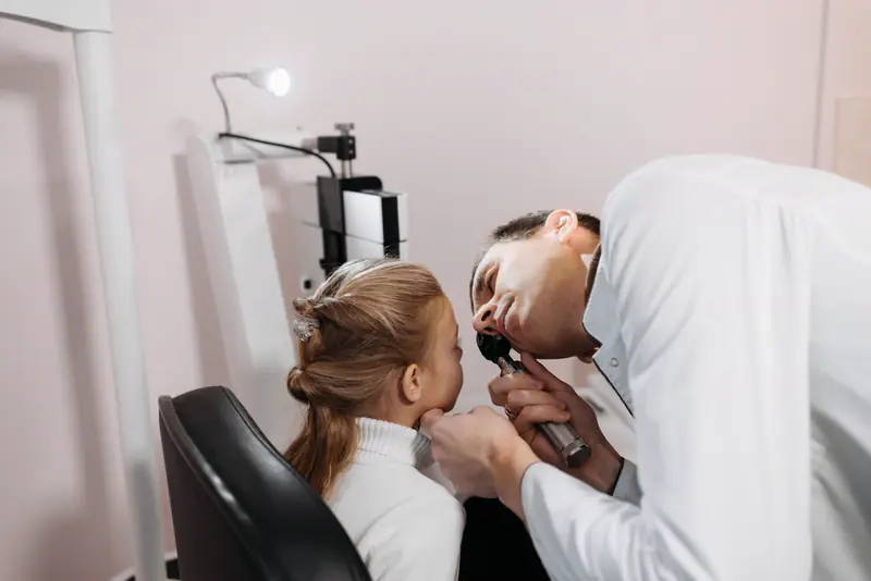 A pediatric provider checks a young girl's ear with an otoscope