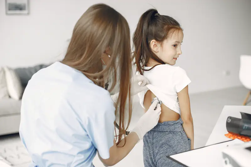 A pediatric provider listens to a young girl's back with a stethoscope