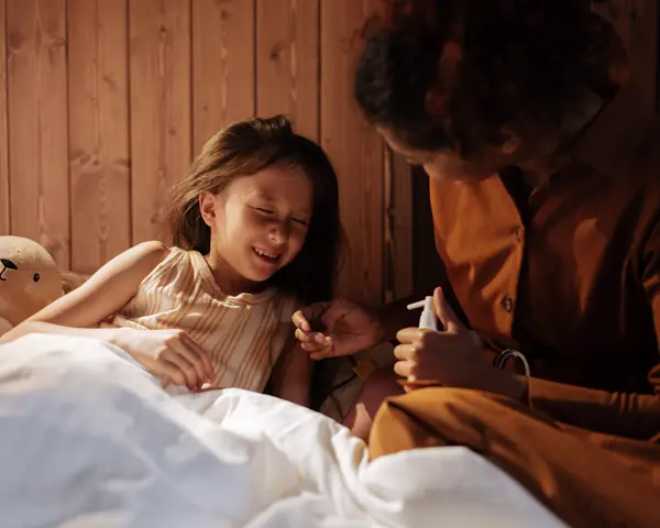 A mother gives medicine to her sick daughter in bed at night