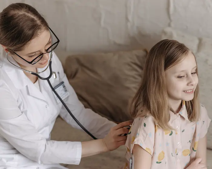 A Little Lanterns pediatrician listens to a smiling girl's breathing with a stethoscope