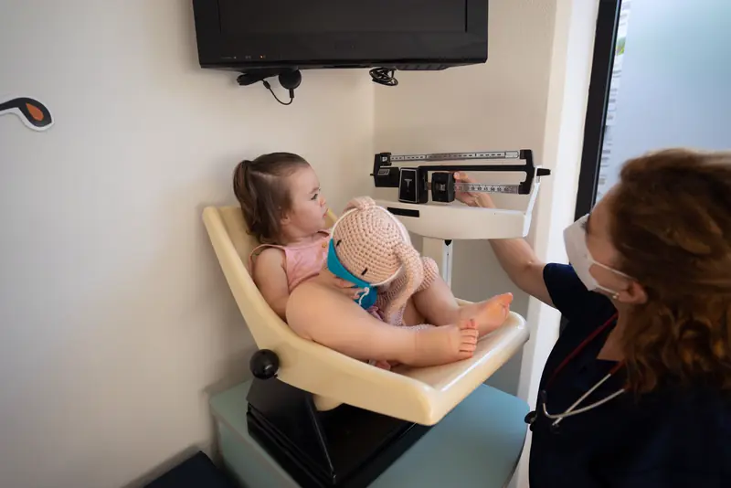 A nurse weighs a little girl on a child-sized scale before her exam