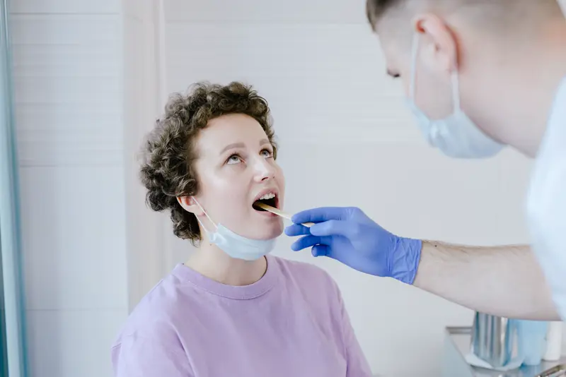 A provider in gloves and a mask takes a throat swab from a patient